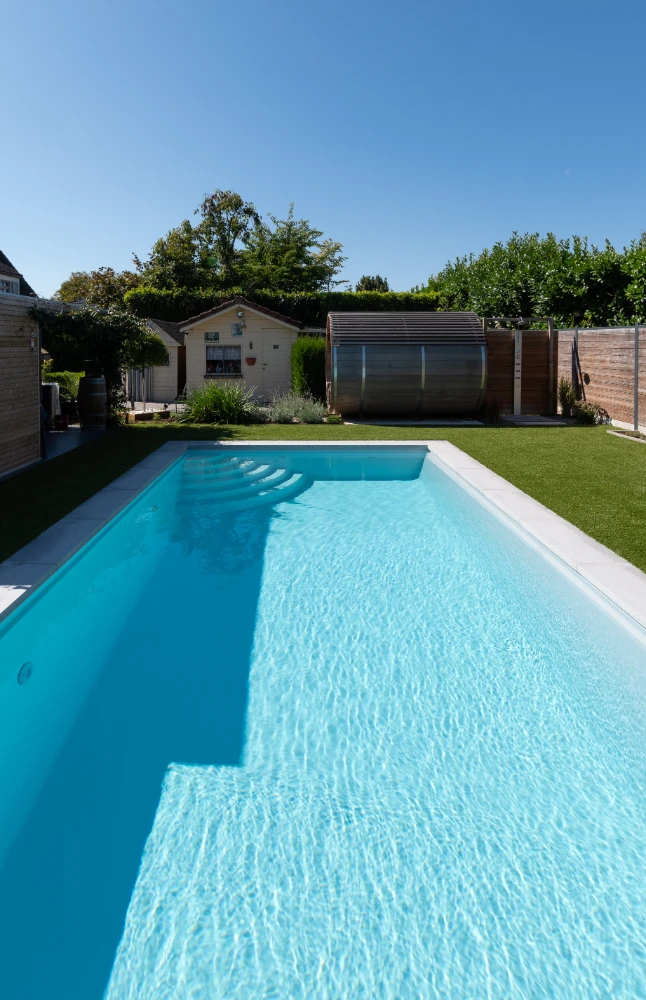 Ein großer Pool mit hellblauem Wasser in einem kleinen Garten, gebaut von D&N-Bewässerunssysteme.